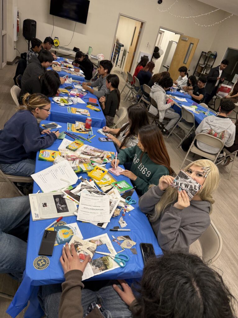 A full room of students making zines at tables during a community workshop