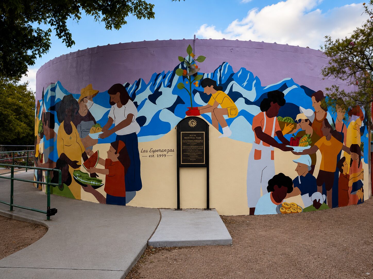Mural wrapped around the historic water tank at Klein Memorial Park — neighbors sharing food beneath the Organ Mountains