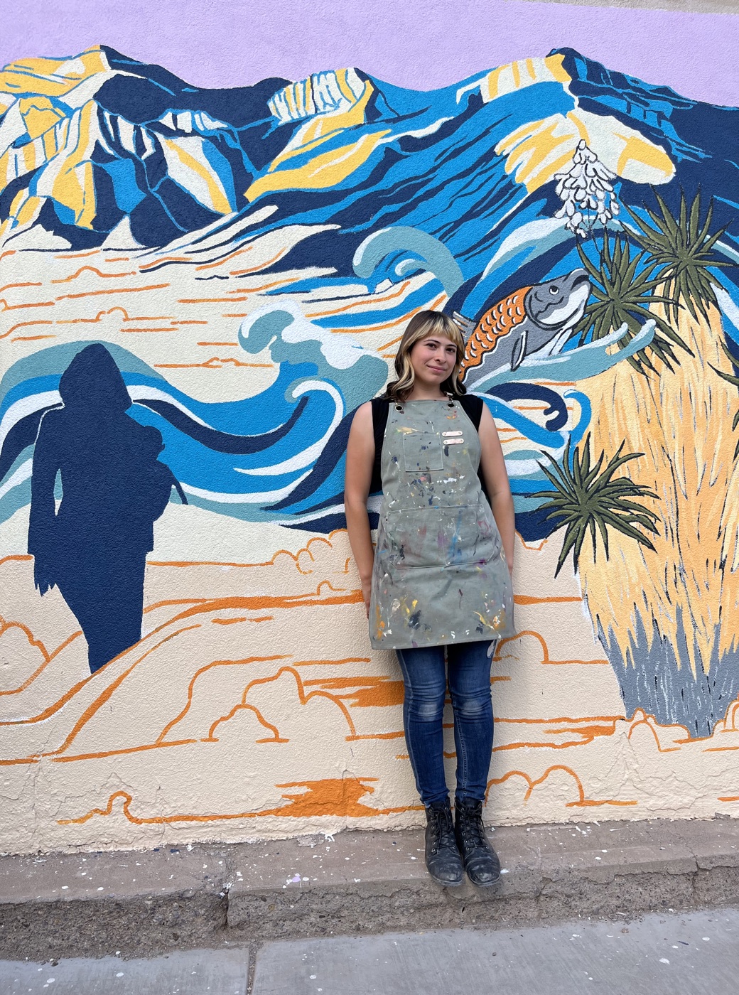 Raquel Madrigal in her paint apron in front of one of her murals